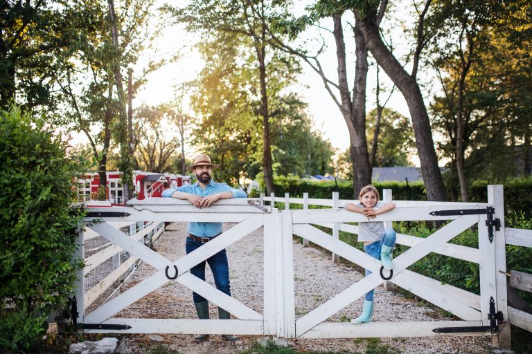 A portrait of father with small daughter outdoors on family farm